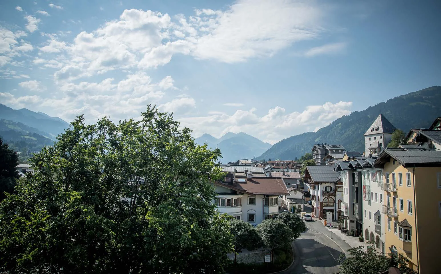 Blick über Kitzbühel im Sommer: Bäume, Häuser, Straße und die Berge im Hintergrund