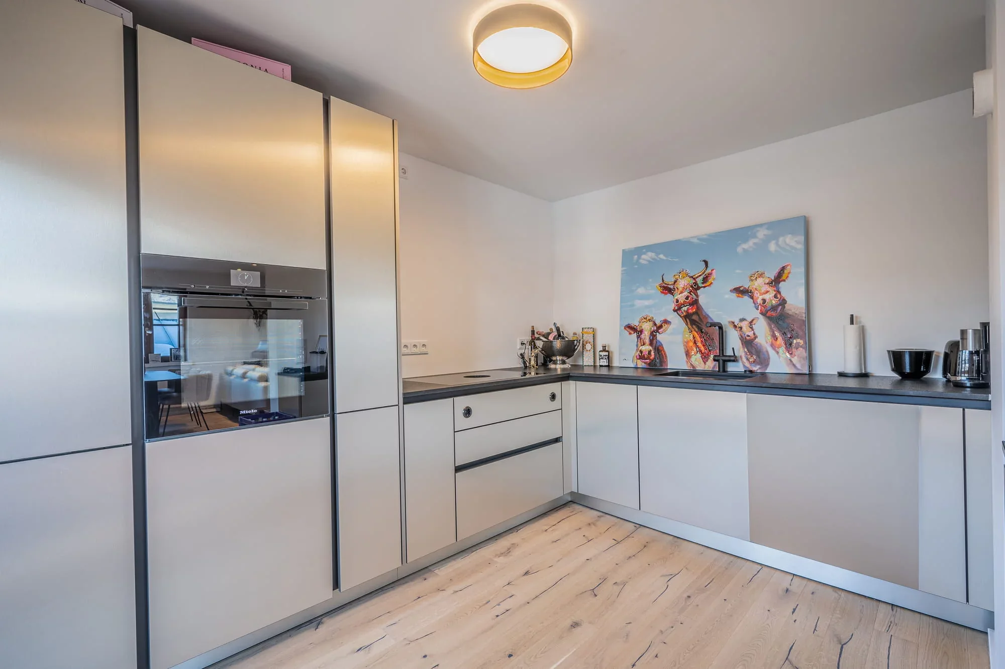Küche mit grifflosen hellen Fronten, dunkler Arbeitsplatte, Einbaubackofen von Miele und Holzboden
